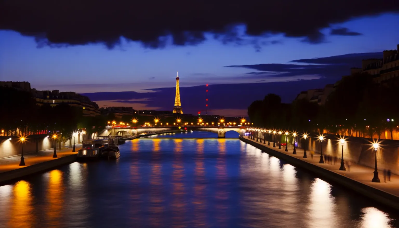 Blick auf den beleuchteten Eiffelturm bei Dämmerung mit der Seine im Vordergrund, umgeben von Straßenlaternen und der Uferpromenade von Paris.